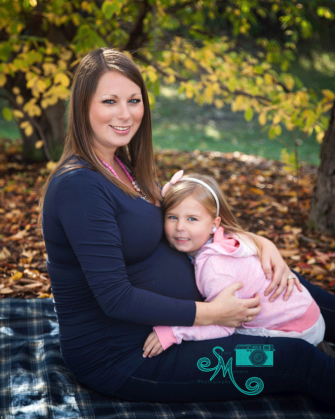 a pregnant mom and her daughter sitting on ground smiling at camera