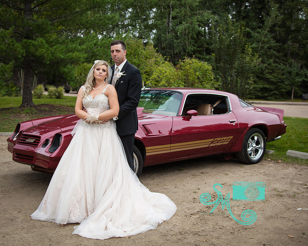 Bride and groom pose in front of a 228 Camero