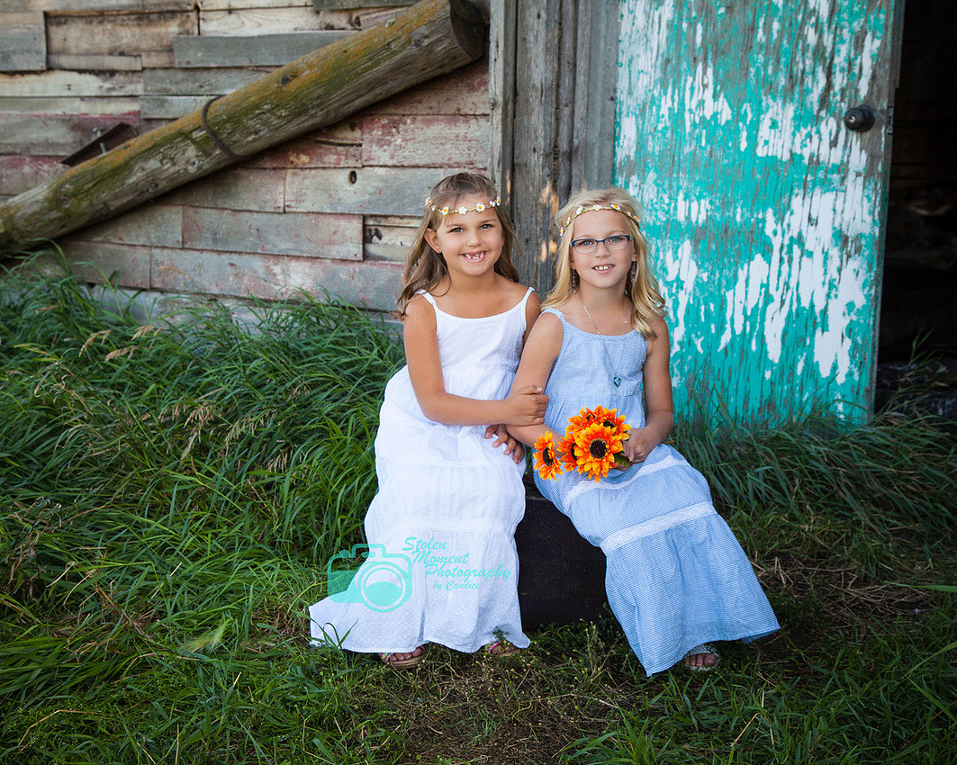 two girls sitting on suitcase outside a barn