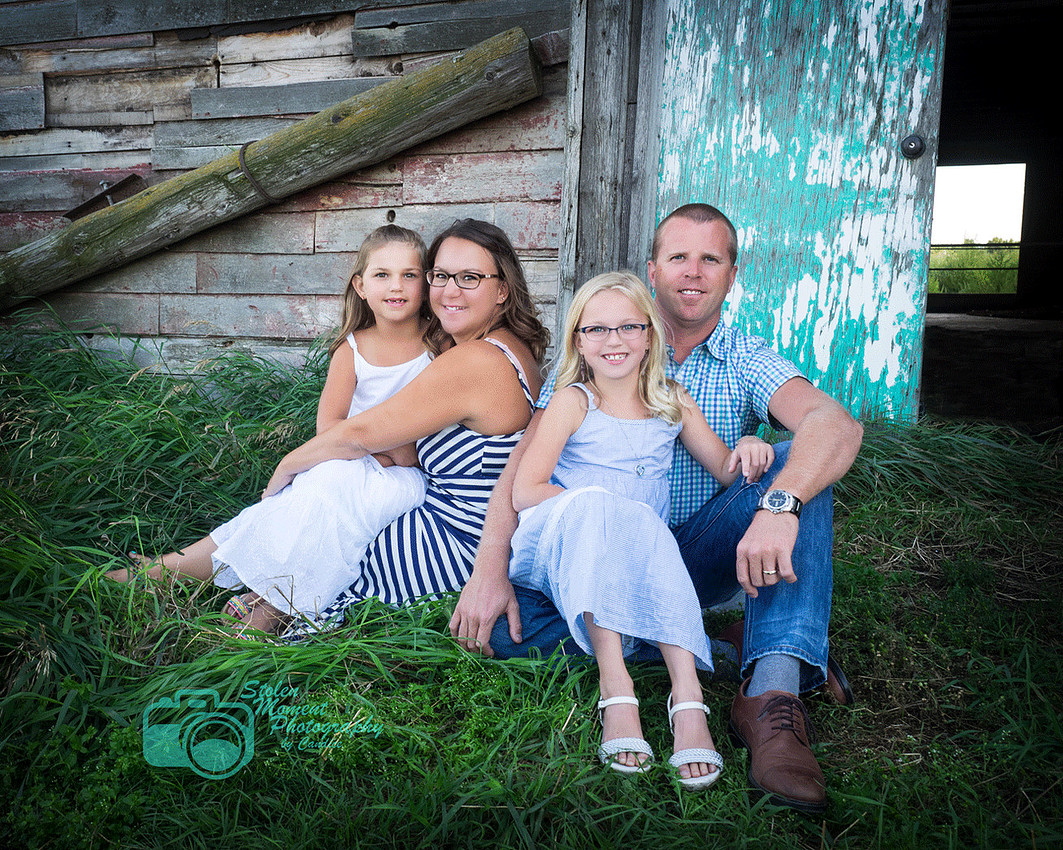 a family of four sitting on grass outside a barn