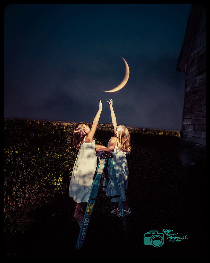 two girls standing on ladder in field reaching for the moon