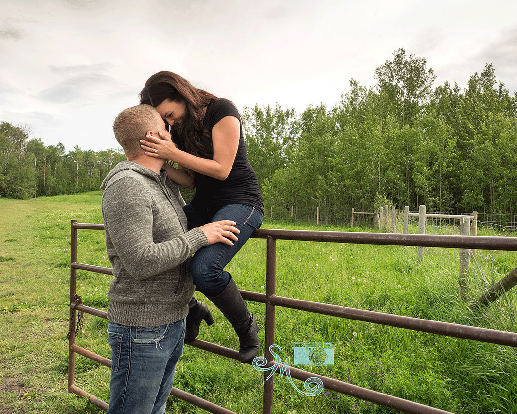 couple snuggling while woman sits on gate