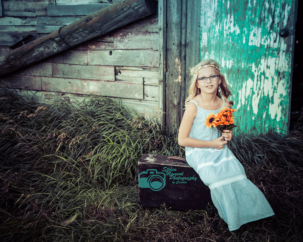 girl sits on suitcase outside barn