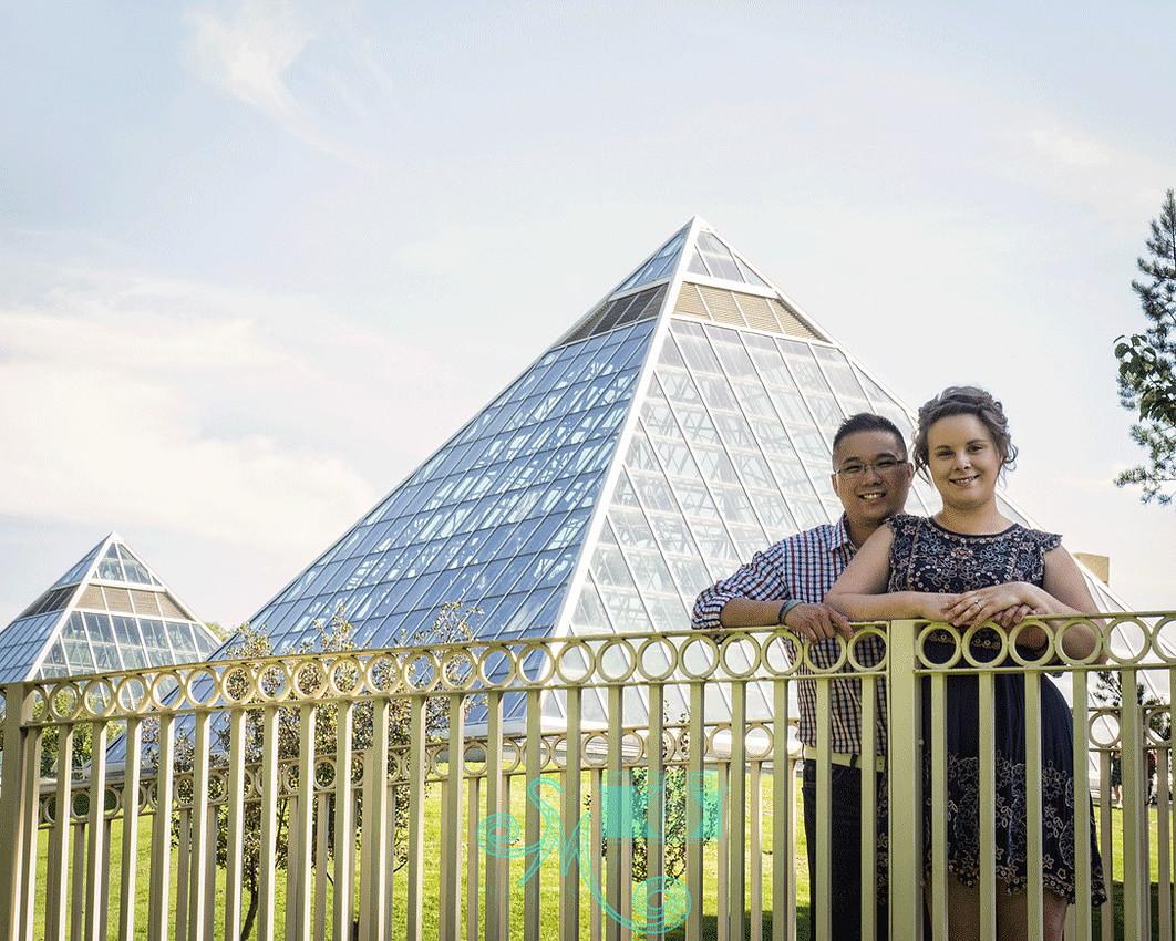 Couple posing on bridge with pyramids of the Muttart Conservatory in the background