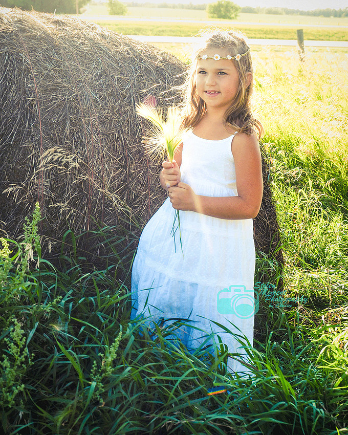 girl stands by bale holding fox tails 