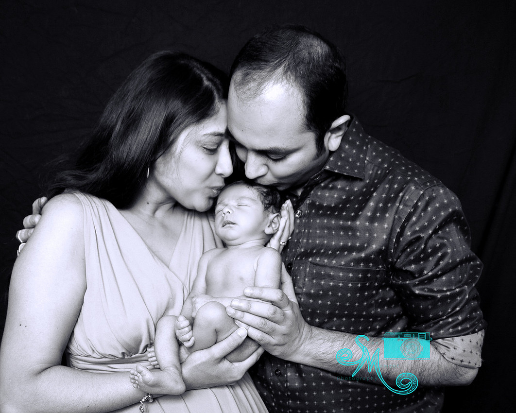 a mom and dad kiss their newborn son on his head