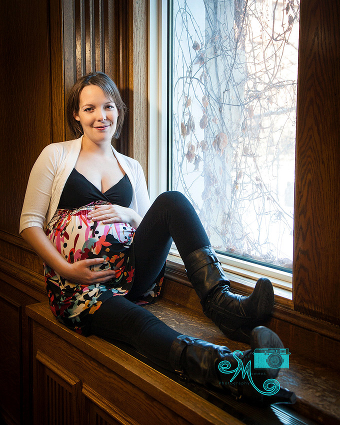 a pregnant lady sits on a window sill looking at the camera