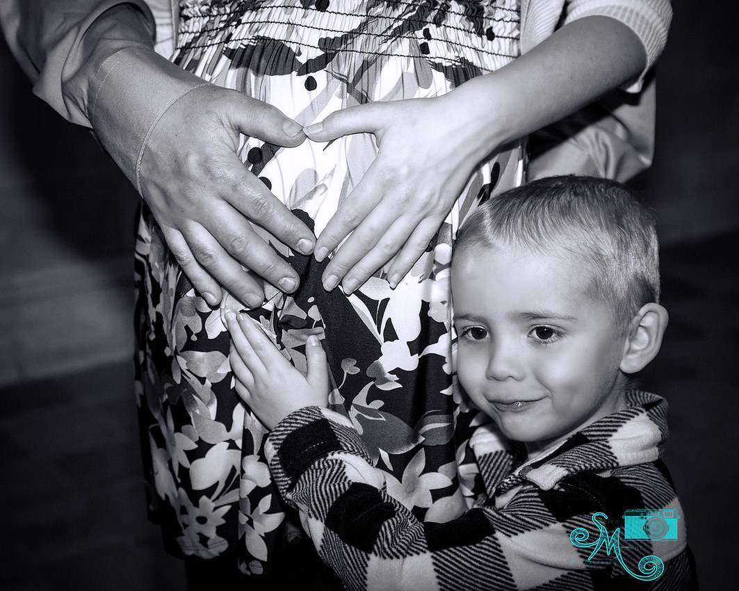 a mom to be and dad form a heart with their hands on her belly while big brother holds on to the belly