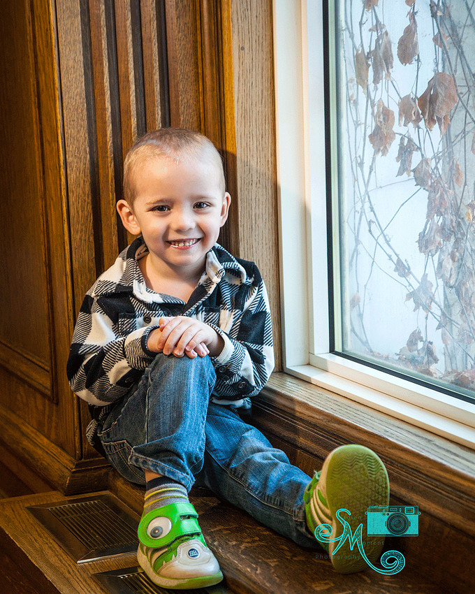 a little boy sits on a window sill smiling at the camera