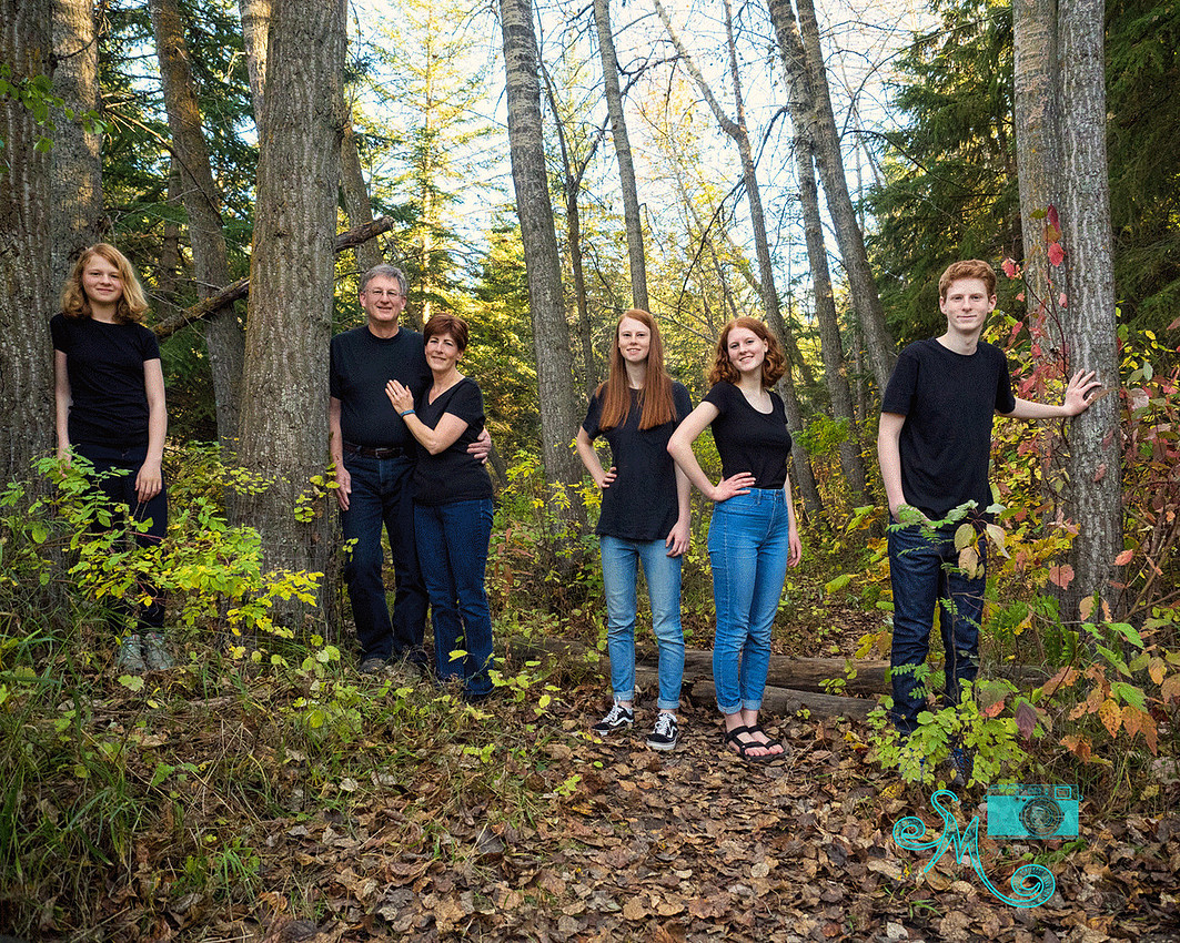 A family of six standing in a forest of tall trees in the fall