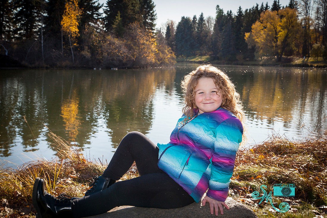 Adorable little girl poses on the rock in front of the lake at Hawrelak park