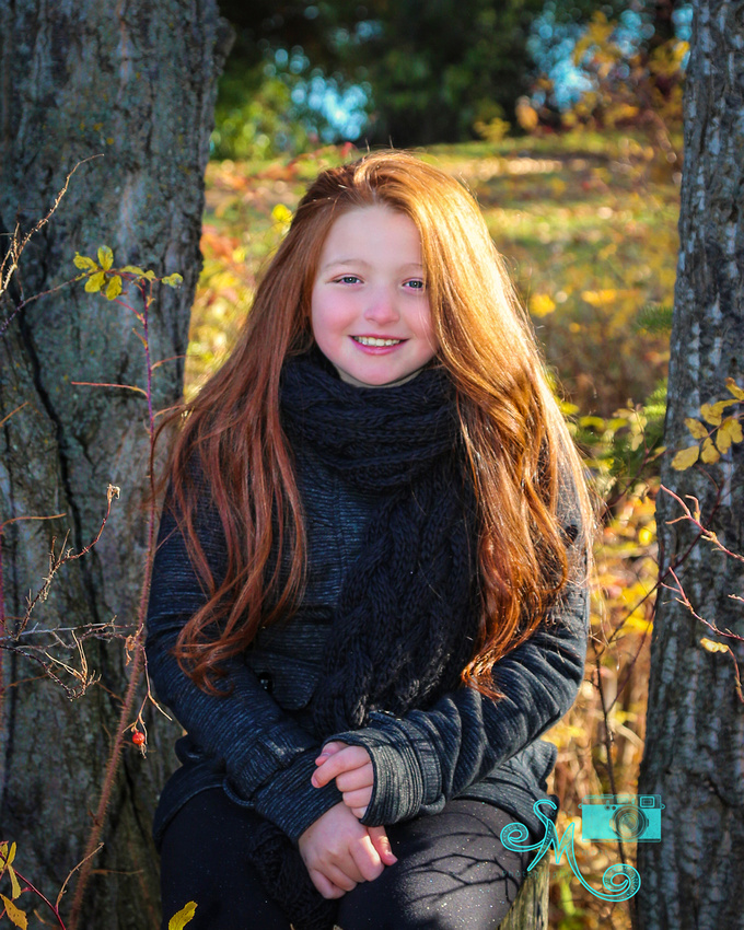 girl sits on a tree stump amongst the fall leaves at Hawrelak park