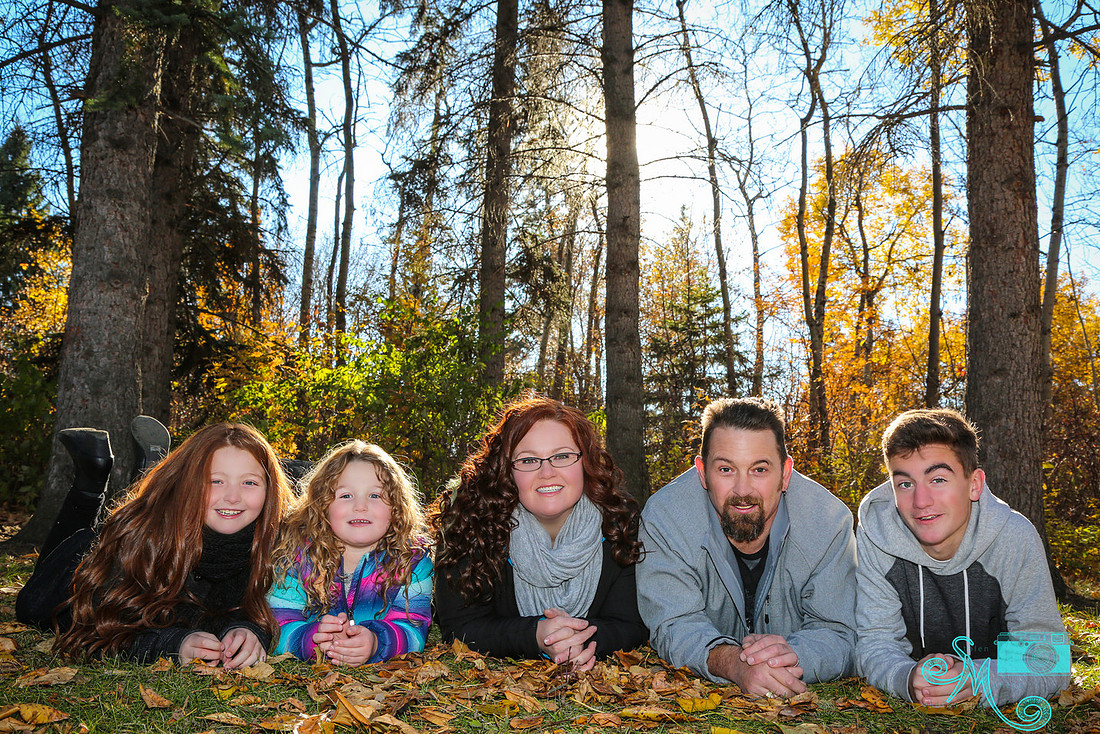 a mom, dad and three children lay on stomachs on the leaves at Hawrelak park