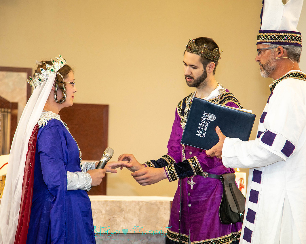 the groom dressed in fourteenth century costume, puts the ring on the bride's finger