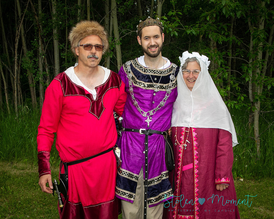 a groom stands with his mother and father, all of whom are dressed in fourteen century costume