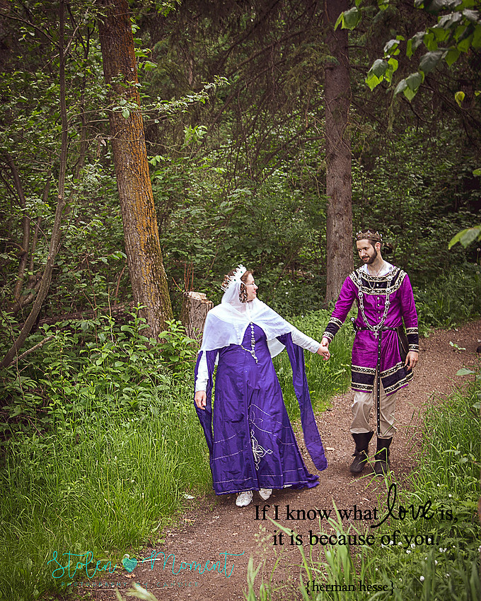 a bride walks ahead of her groom holding his hand and looking back at him on a path in the ravine "forest" and both are dressed in medieval costume