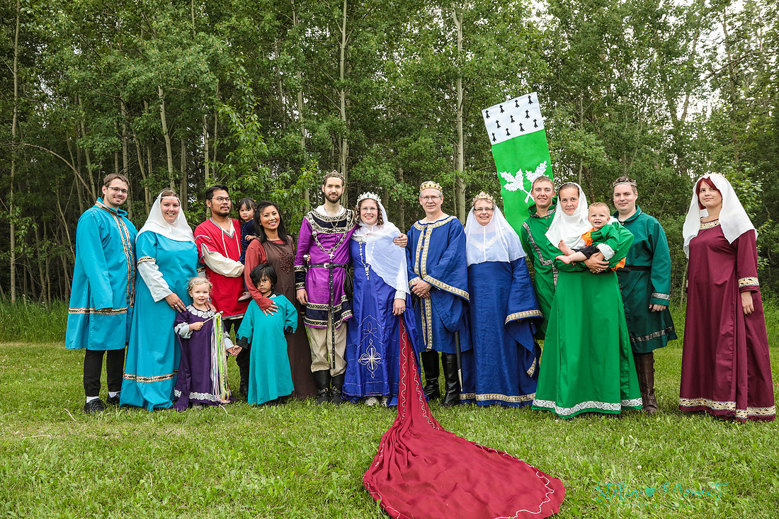 the bride and groom stand with the bride's parents, siblings and their families with one member holding the family's coat of arms - all the people are dressed in fourteenth century costume