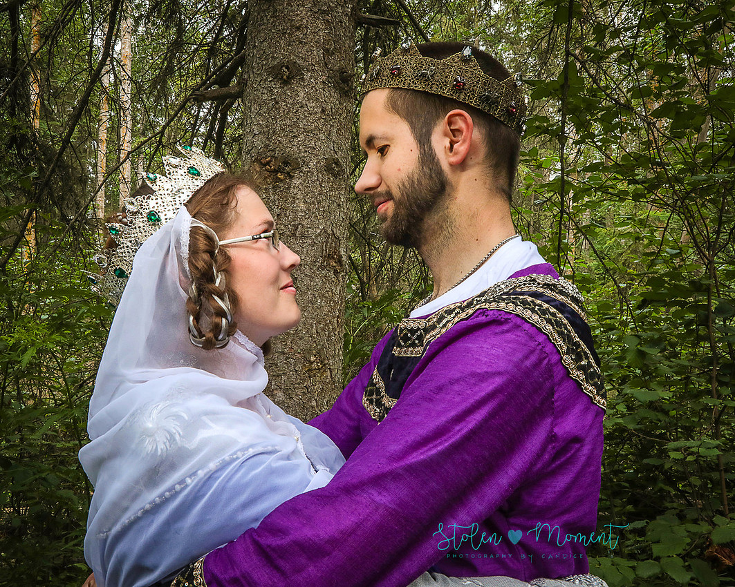 the bride and groom dressed in medieval costumes look into each other's eyes while standing in a "forest"