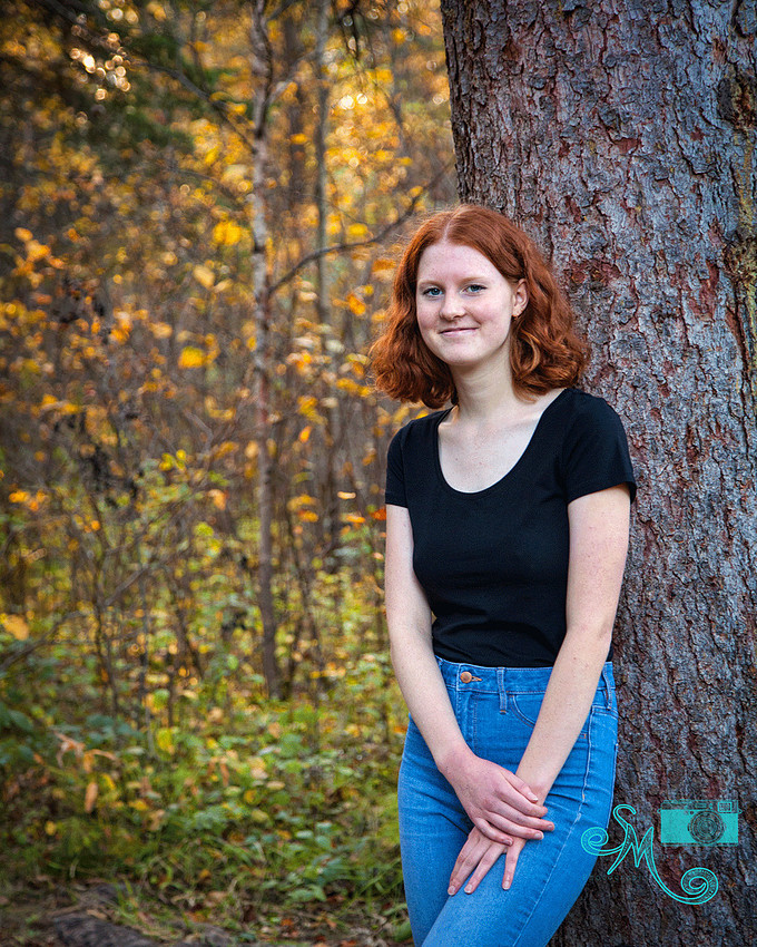 a teenage girl posing against a tree with fall leaves in the background