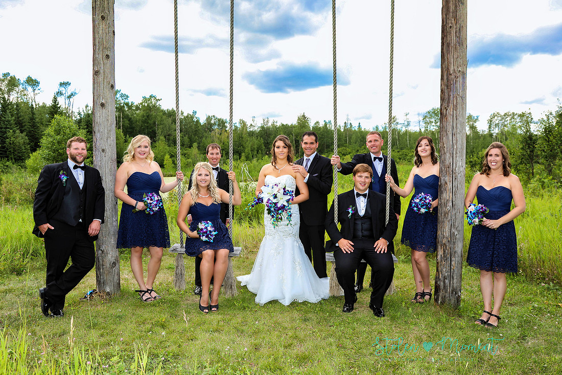 a wedding party of ten stand and sit around a wooden swing set at Hastings Lake Gardens, Sherwood Park