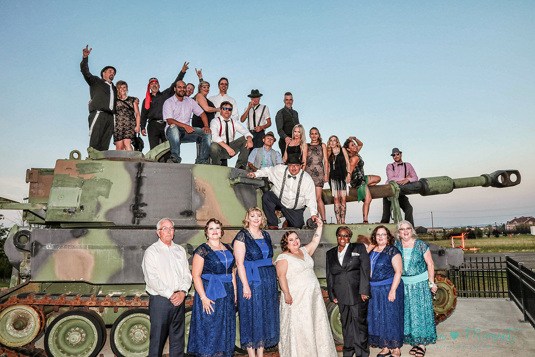the entire wedding party and almost every guest pose on and in front of a large army tank outside the Kingsway Legion 