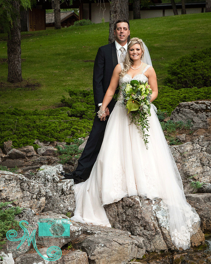 Bride and groom holding hands standing on rocks by waterfall in Devonian Gardens