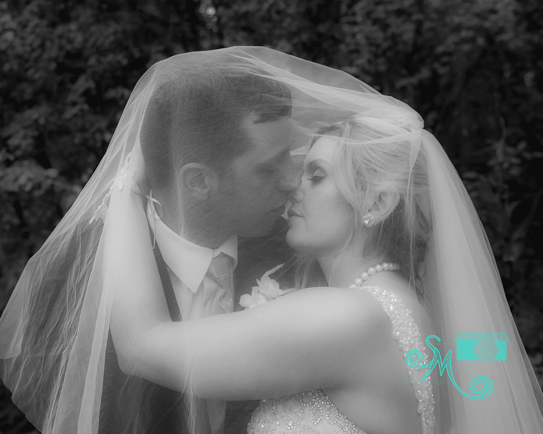 black and white photo of bride and groom about to kiss under her veil