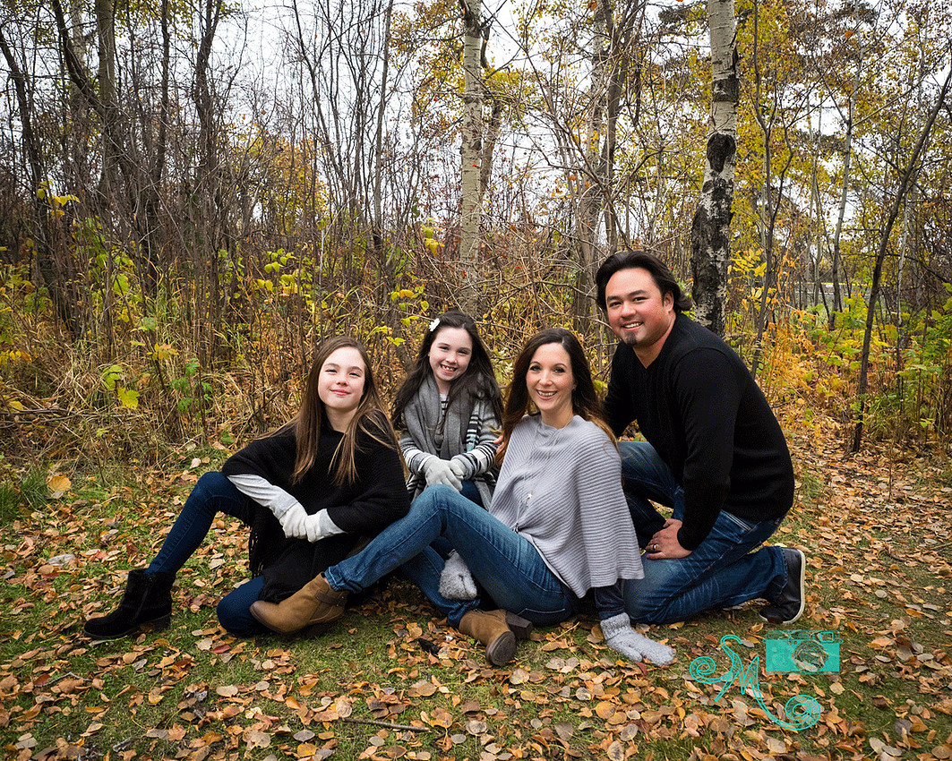 a family of four sit on the ground on a fall day