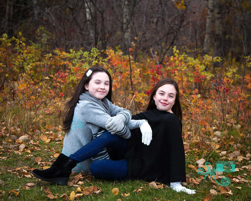 two sisters sit on the ground in the fall