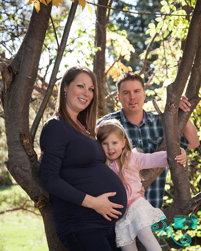 dad, pregnant mom and first born pose against a fall tree