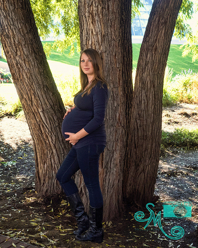 mom to be stands in front of a big tree