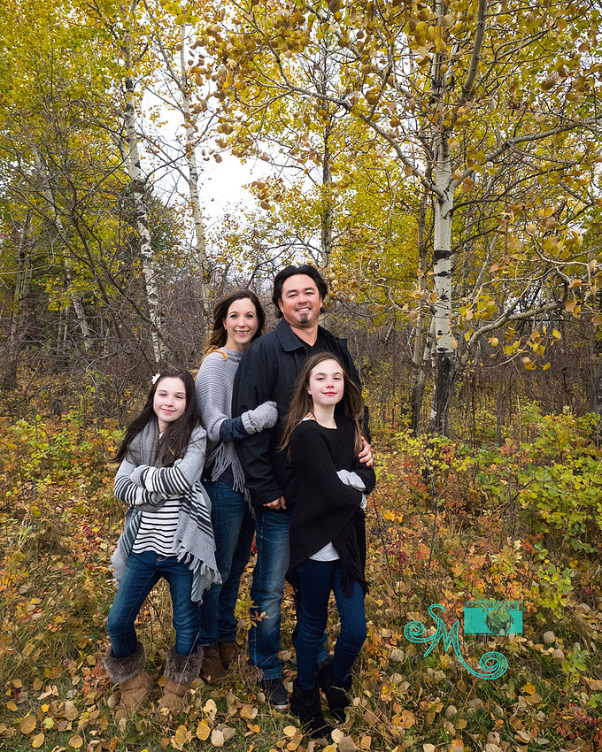 a family of four stand amongst fall coloured trees in Sherwood Park