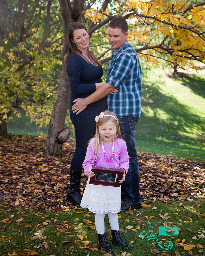 mom and dad looking at their little girl holding unborn siblings ultrasound photo