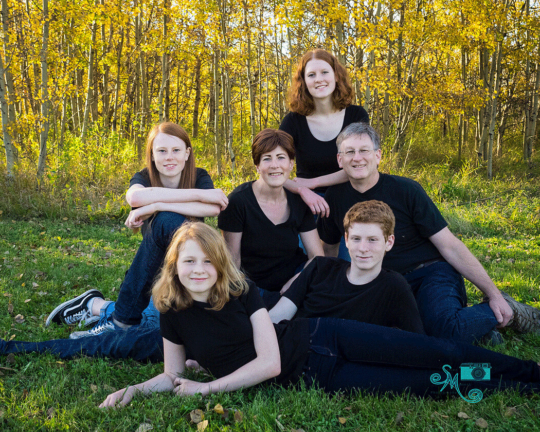 a family of six poses on the grass in front of a bunch of yellow leaved trees in Whitemud creek ravine in Edmonton