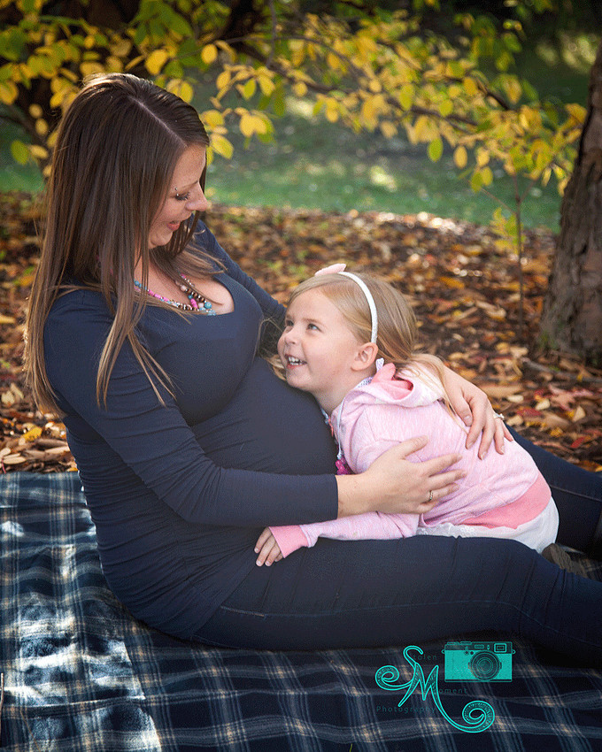 a little girl sits on her pregnant mom's lap smiling up at her